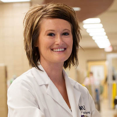 A nurse smiles while standing in a hospital hallway.